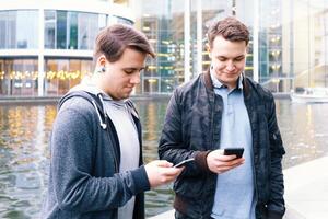 två mobil telefon Beroende manlig tonåringar stående tillsammans ser på smartphone foto