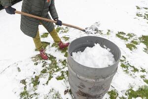 medelålders kvinna är samlar snö i en tunna med en spade, naturlig Resurser foto