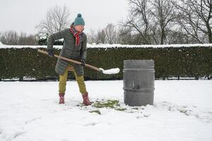 medelålders kvinna är samlar snö i en tunna med en spade, naturlig Resurser foto