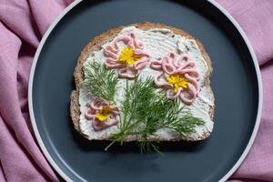 kreativ smörgås med mjuk ost och rosa pasta tarama gröna, blommor foto