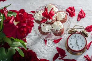 fortfarande liv i engelsk stil med scharlakansrött pioner och röd sammet muffins med på en tallrik, te tid på röd antik klocka foto