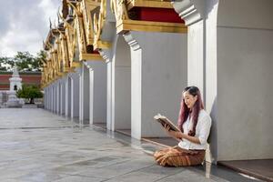 asiatisk buddist kvinna är läsning sanskrit gammal tripitaka bok av herre buddha dhamma undervisning medan Sammanträde i tempel till sång och dyrkan inuti de kloster foto