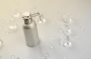 kvinna parfym silverren flaska, mål fotografera av metallisk parfym flaska i is kuber och vatten på vit tabell. se från ovan. attrapp produkt Foto, begrepp av friskhet foto