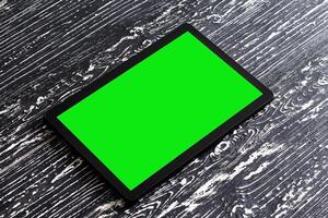 svart läsplatta med grön skärm på en trä- tabell falsk upp. kopia Plats krom nyckel visa. foto