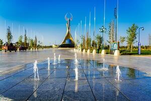 bekistan, Tasjkent - april 25, 2023 fontäner i en bakgrund av monument av oberoende i de form av en stele med en humo fågel mot en blå himmel i de ny uzbekistan parkera. foto