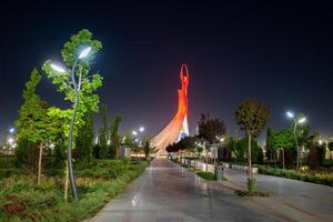 uzbekistan, Tasjkent - Maj 5, 2023 upplyst monument av oberoende i de form av en stele med en humo fågel, fontäner och vinka flaggor i de ny uzbekistan parkera på nattetid. foto