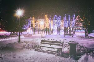 vinter- parkera på natt med jul dekorationer, lysande lyktor, trottoar täckt med snö och träd. årgång filma estetisk. foto