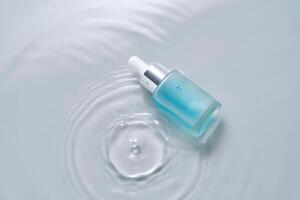 flaskor av kosmetika med en dropper i vatten på en blå bakgrund. foto