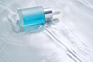 flaskor av kosmetika med en dropper i vatten på en blå bakgrund. foto