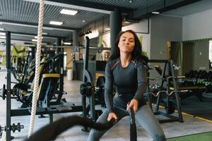 kondition på de tågvirke. skön kvinna i Gym arbetssätt ut med rep. ung kvinna Träning hård foto