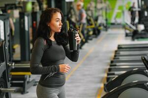 ung skön kvinna dricka vatten i sporter Gym. foto