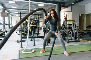 kondition på de tågvirke. skön kvinna i Gym arbetssätt ut med rep. ung kvinna Träning hård foto