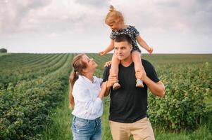 de dotter kramas föräldrar på natur. mamma, pappa och flicka småbarn, promenad i de gräs. Lycklig ung familj utgifterna tid tillsammans, utanför, på semester, utomhus. de begrepp av familj Semester foto