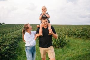 Lycklig familj gående i de parkera. mamma, pappa och dotter promenad utomhus, föräldrar innehav de bebis flickans händer. barndom, föräldraskap, familj obligationer, äktenskap begrepp. foto