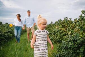 Lycklig familj gående i de parkera. mamma, pappa och dotter promenad utomhus, föräldrar innehav de bebis flickans händer. barndom, föräldraskap, familj obligationer, äktenskap begrepp. foto