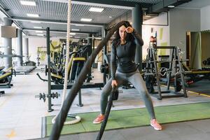 Söt latinamerikan ung kvinna håller på med några crossfit övningar med en rep på en Gym. foto