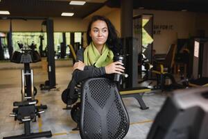 ung kvinna dricka vatten och tar en ha sönder efter träna i Gym foto