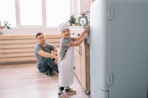 ung man och hans son med ugn ark i kök. far med liten son på de kök. foto