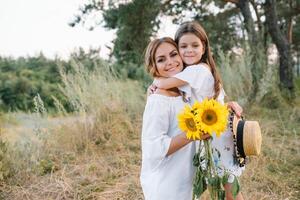 glad mor och henne liten dotter har roligt tillsammans i de sommar bakgrund. Lycklig familj i de natur bakgrund. söt flickor med färgrik blommor foto