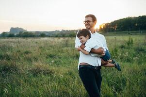 stilig pappa med hans liten söt son är har roligt och spelar på grön gräs- gräsmatta. Lycklig familj begrepp. skönhet natur scen med familj utomhus- livsstil. familj vilar tillsammans. fäder dag. foto