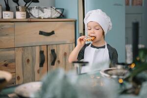 ung Lycklig mamma och henne bebis laga mat småkakor på Hem i de kök. jul hemlagad pepparkaka. söt pojke med mor i vit enhetlig och hatt kokta choklad småkakor. foto