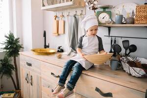 ung Lycklig mamma och henne bebis laga mat småkakor på Hem i de kök. jul hemlagad pepparkaka. söt pojke med mor i vit enhetlig och hatt kokta choklad småkakor. foto