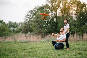 far, mor och son spelar med leksak flygplan i de parkera. vänlig familj. människor har roligt utomhus. bild tillverkad på de bakgrund av de parkera och blå himmel. begrepp av en Lycklig familj foto