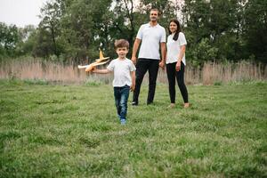 far, mor och son spelar med leksak flygplan i de parkera. vänlig familj. människor har roligt utomhus. bild tillverkad på de bakgrund av de parkera och blå himmel. begrepp av en Lycklig familj foto