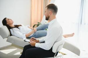 psykolog tar anteckningar under terapi session med ledsen ung kvinna i hans kontor. kopia Plats foto