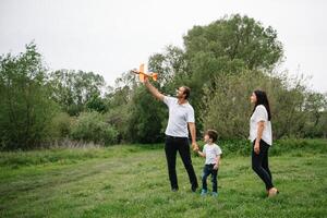 far, mor och son spelar med leksak flygplan i de parkera. vänlig familj. människor har roligt utomhus. bild tillverkad på de bakgrund av de parkera och blå himmel. begrepp av en Lycklig familj foto