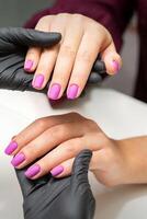 undersökning av välskött fingernaglar. händer av manikyr bemästra i svart handskar granskning kvinna rosa naglar i manikyr salong. foto