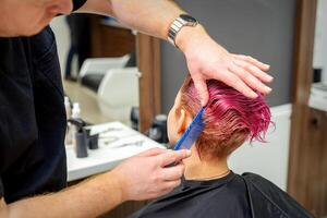 händer av frisör kammande hår framställning kort rosa frisyr för en ung caucasian kvinna i en skönhet salong. foto