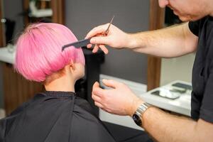 händer av frisör kammande hår framställning kort rosa frisyr för en ung caucasian kvinna i en skönhet salong. foto
