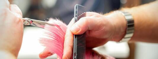 kvinna har en ny frisyr. manlig hårstylist skärande rosa hår med sax i en hår salong, stänga upp. foto