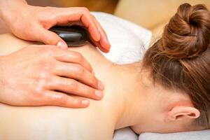 varm sten massage terapi. caucasian ung kvinna få en varm sten massage på tillbaka på spa salong. foto