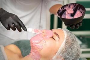 de kosmetolog applicering ett alginat mask till de ansikte av en ung kvinna i en skönhet salong. foto