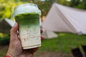 hand innehav iced grön te matcha latte med camping bakgrund foto