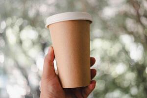 hand innehav ett brun kaffe papper kopp med en lock. foto