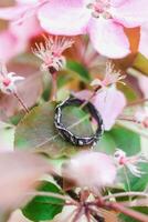 skön silver- handgjort ringa på en gren av äpple träd med rosa blommor. hantverk dyrbar Artikel. Smycken Tillbehör. foto