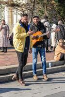 istanbul, Kalkon - december 29, 2022. två män, ett spelar gitarr och sång, de Övrig lyssnande spänt på en stad gata hörn. foto