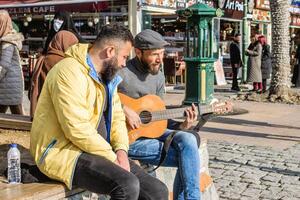 istanbul, Kalkon - december 29, 2022. två män är Sammanträde på bänk förbi de gata och ett av dem spelar gitarr. foto