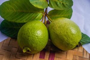 guava isolerat. samling av guava frukt med gulaktig grön hud och löv isolerat på vit bakgrund med vävd bambu som en bas. foto