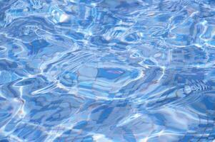 abstrakt bakgrund av blå vatten lysa skarpt på de yta i en slå samman, fontän på en solig dag. foto