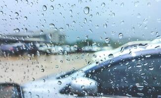 regn droppar på bil glas fönster yta av förarens dörr medan parkerad i utomhus parkering massa under regnig väder foto