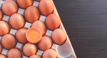 platt lägga av färsk brun kyckling ägg som ett knäckt ägg med äggula i papper ägg bricka på trä- kök bordsskiva, topp se med kopia Plats foto