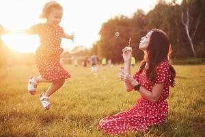 liten flicka med bubblor med sin mamma i parken vid solnedgången. foto