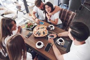 god pizza på bordet, med en grupp unga leende människor som vilar i puben foto