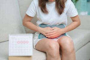 menstruation period cykel av en gång i månaden och magont begrepp. kvinna har buk smärta med varm vatten flaska och kalender, sjukdom kvinna lida från premenstruell värk och kropp hälsa problem foto