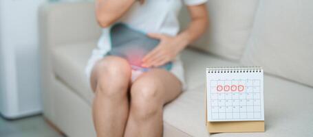menstruation period cykel av en gång i månaden och magont begrepp. kvinna har buk smärta med varm vatten flaska och kalender, sjukdom kvinna lida från premenstruell värk och kropp hälsa problem foto