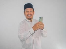moslem asiatisk man som visar Wow uttryck medan innehav hans mobil telefon foto